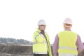 Male engineer using mobile phone while standing with colleague at construction site against clear sky