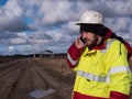 Male Engineer in white helmet talking by modern phone at field with plans building windmils Royalty Free Stock Photo