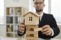 Business man removes blocks from under toy house as concept of unstable real estate market