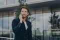 Male entrepreneur talks via phone solves urgent problems poses near business center Royalty Free Stock Photo