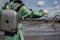 A male environmentalist in a green protective suit and gas mask takes a sample of water in a polluted lake for research