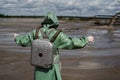 A male environmentalist in a green protective suit and gas mask takes a sample of water in a polluted lake. Waste from