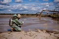 A male environmentalist in a green protective suit and gas mask takes a sample of water. The scientist is doing a