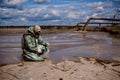 A male environmentalist in a green protective suit and gas mask takes a sample of water. The scientist is doing a