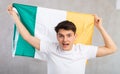 Male fan in casual clothes holds canvas of national Irish flag in hands and chants popular slogan