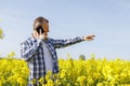 A male farmer agronomist stands in a field of flowering rapeseed and talks on the phone. Checking the quality of the