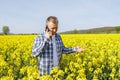 A male farmer agronomist stands in a field of flowering rapeseed and talks on the phone. Checking the quality of the