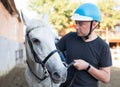 Male farmer in helmet standing with white horse at stable outdoor Royalty Free Stock Photo