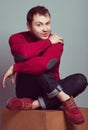 Male fashion concept. Portrait of young man wearing trendy casual purple sweater, blue jeans and purple shoes. Guy sitting on a Royalty Free Stock Photo