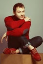 Male fashion concept. Portrait of young man wearing trendy casual purple sweater, blue jeans & red chamois shoes. Guy sitting on Royalty Free Stock Photo