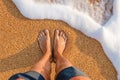 male feet barefoot on the waves of sea foam on a sandy golden beach on a summer day. top view of male legs in shorts and