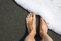 Male feet on the black volcanic sand covers with white sea foam. Minimalism. Geometric. Diagonal Royalty Free Stock Photo