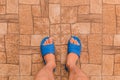 Male feet in blue house slippers stand on brown tile floor with abstract stone pattern texture background, top view Royalty Free Stock Photo