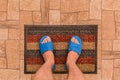 Male feet in blue house slippers stand on a foot mat on a brown tiled floor texture background, top view Royalty Free Stock Photo