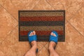 Male feet in blue house slippers stand on a foot mat on a brown tiled floor texture background, top view Royalty Free Stock Photo