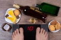 Male feet on digital scales with word no on screen. Bottles and glasses of alcohol, plates with sweet food.