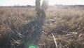 Male feet of ukrainian soldiery going in brown boots through dry grass at countryside. Legs of young army man in