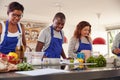 Male And Female Adult Students Preparing Ingredients For Dish In Kitchen Cookery Class