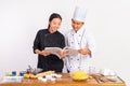 male and female chefs using cookbooks standing near table