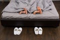 Male and female feet under grey blanket, near two pairs of white Royalty Free Stock Photo