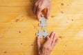 Male and female hand joining two matching puzzle pieces over yellow wooden background Royalty Free Stock Photo