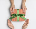 Male and female hands holding gift box in striped craft paper with green bow on light background flat lay top view. Present for