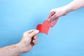 Male and female hands are holding a red paper heart on a blue background, concept of love Royalty Free Stock Photo