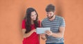 Male and female hipsters using digital tablet against orange background