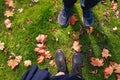 Male and female legs in sneakers and boots standing on ground with yellow autumn leaves Royalty Free Stock Photo