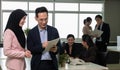 Male and female office employee looking at digital tablet PC while standing in open space office with blurred colleagues working Royalty Free Stock Photo