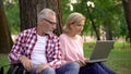 Male and female pensioners choosing hotel for vacation on laptop resting in park