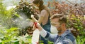 Male and female professional gardeners spraying fertilizer on plants