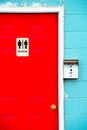 And female signs on red wooden restroom door of blue stone building Royalty Free Stock Photo