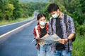 Male and female tourists wear medical masks and look at the map on the street