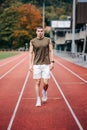 Male figure striding confidently across an orange running track in a stadium setting