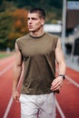 Male figure striding confidently across an orange running track in a stadium setting