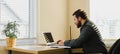 Male financier sitting at desk and using laptop at cabinet.