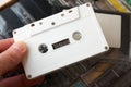 Male fingers hold white audio cassette against box with many tapes