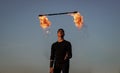 Male fire performer manipulate with flaming baton on blue sky outdoors, man