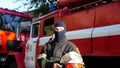 Male firefighter taking off helmet and balaclava against background of a fire engine. Portrait of young fireguard in