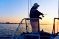 A male fisherman with a spinning rod in his hand catches fish from a boat at dawn.