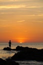 Male fisherman standing on the rocks during sunset