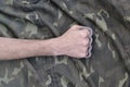 Male fist with brass knuckles on the background of a camouflage jacket. The concept of skinhead culture, handmade melee weapons