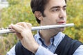 A male flutist playing outdoors.