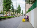 A male food delivery courier sits on a bench on a city street