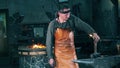 Male forger stands near an anvil, holding a hammer. Blacksmith forging iron in workshop.