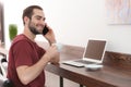 Male freelancer drinking coffee while talking on phone in home office