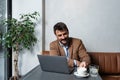 Male freelancer sitting at a restaurant table, drinking coffee and working on a laptop computer. Expatriate man in cafeteria doing Royalty Free Stock Photo