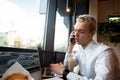 Male freelancer swears on the phone. Upset blonde man in white shirt. Remote work concept. Modern laptop on table Royalty Free Stock Photo