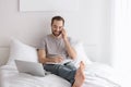 Male freelancer talking on phone while working in bed